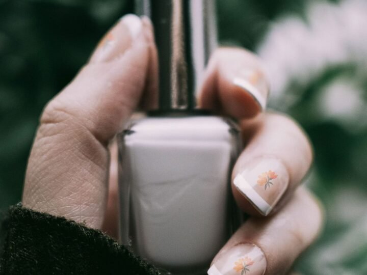 Natural short manicure with delicate floral nail art holding a nail polish bottle