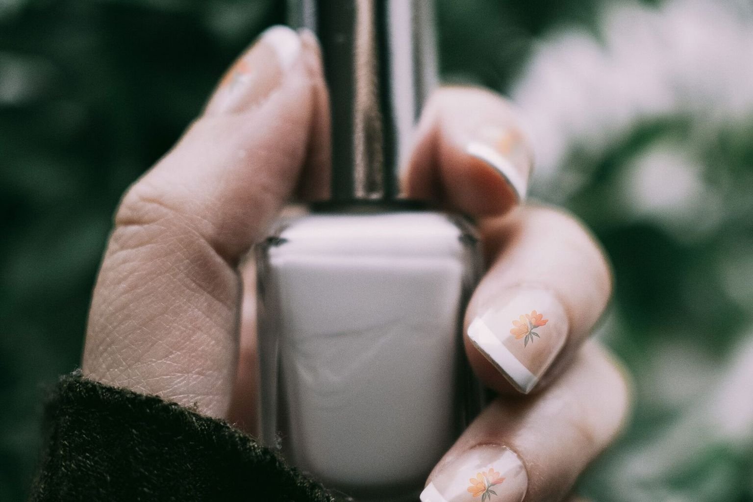 Natural short manicure with delicate floral nail art holding a nail polish bottle