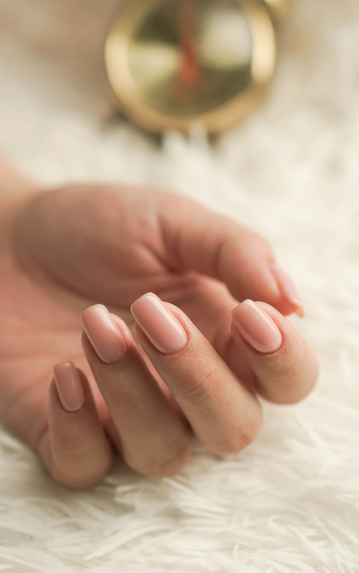 Hand with a clean light pink manicure on a soft neutral background