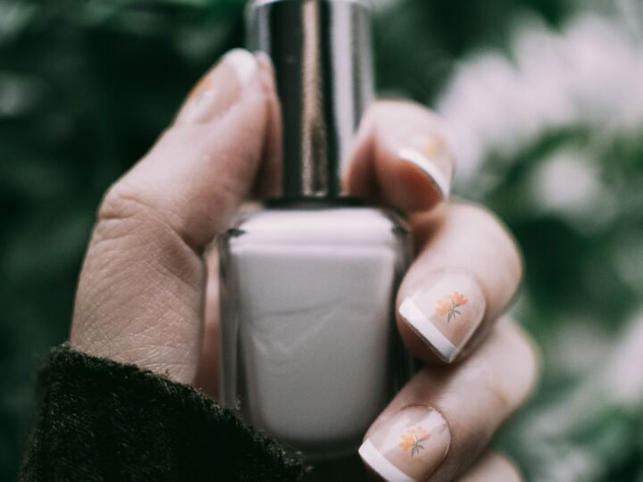 Natural short manicure with delicate floral nail art holding a nail polish bottle