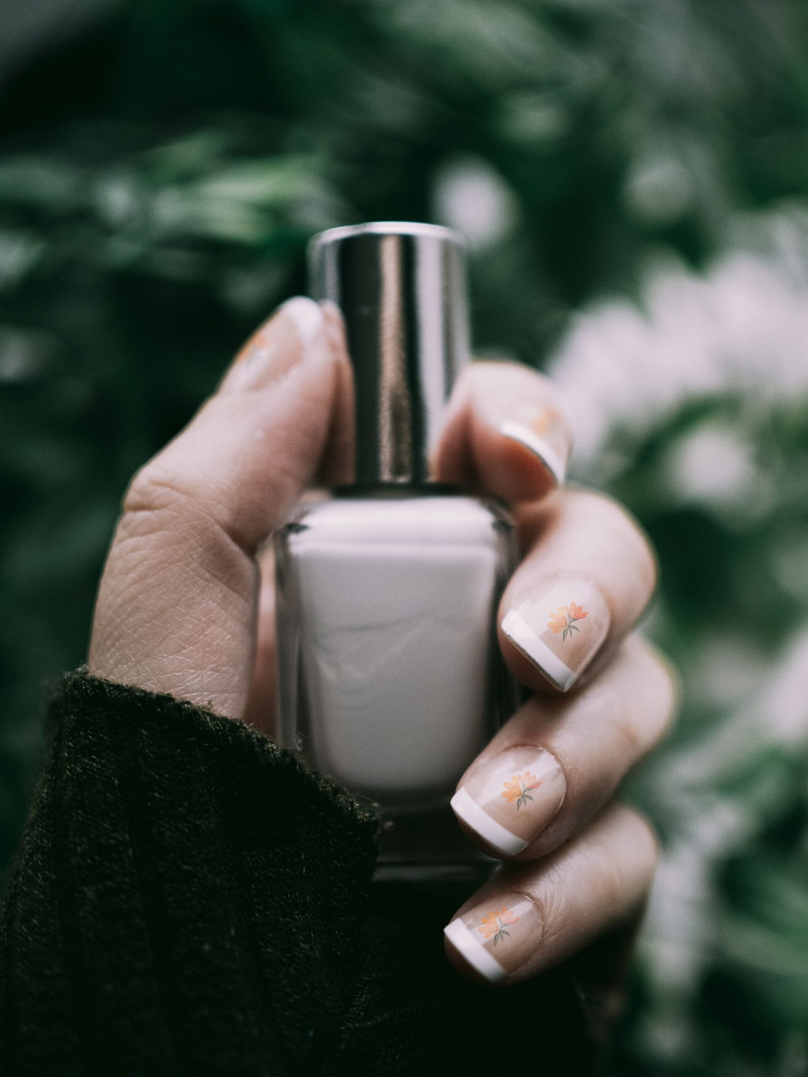 Natural short manicure with delicate floral nail art holding a nail polish bottle